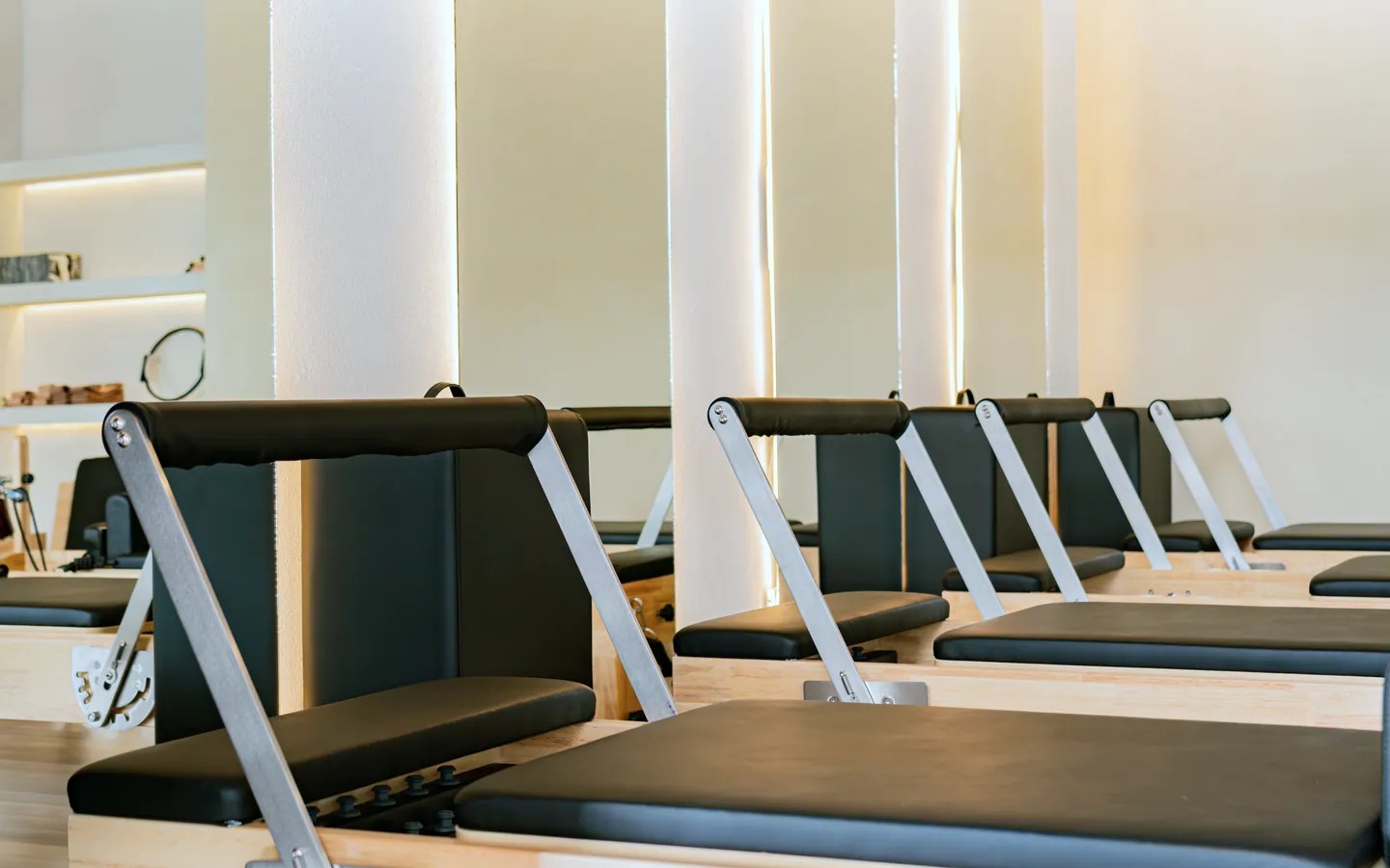 Close view of reformer pads, a steel footbar and timber frames, with an arched alcove glowing behind them.
